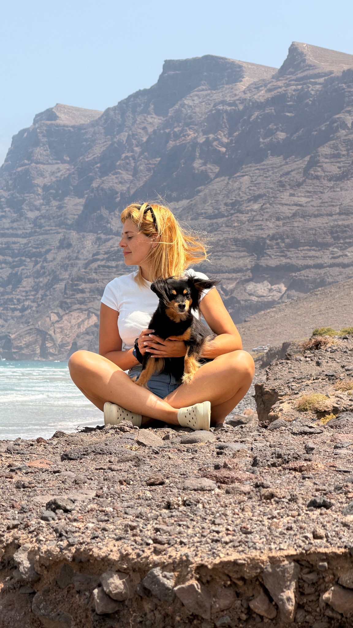De perfil abrazando al perrito con la pared del Risco de Famara al fondo