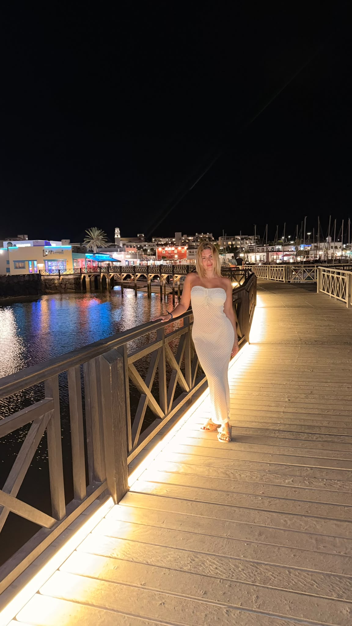 De noche en la pasarela iluminada del puerto, vestido blanco