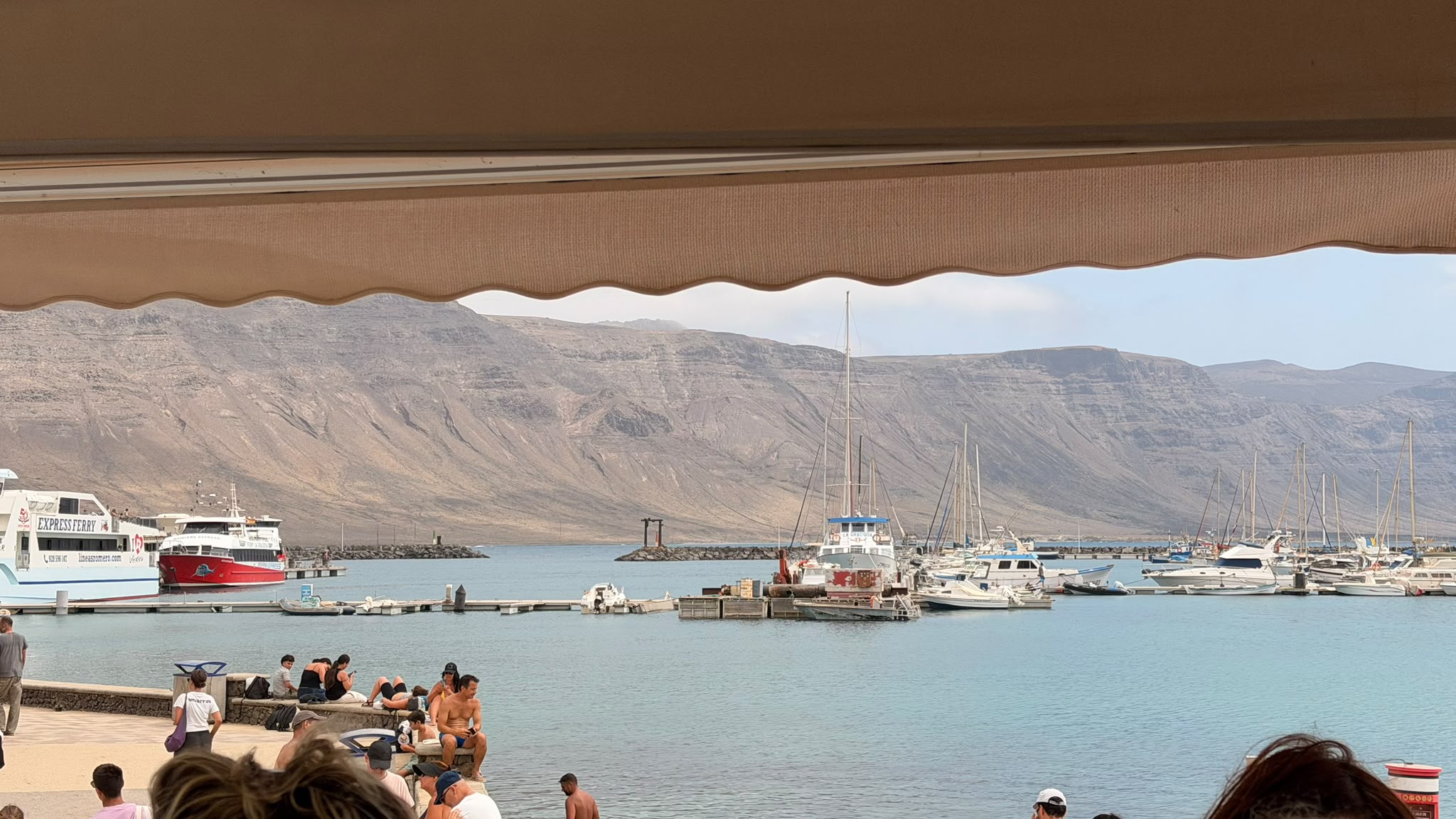 Vista del puerto de Caleta del Sebo desde la terraza de un restaurante, con el Risco de Famara al fondo
